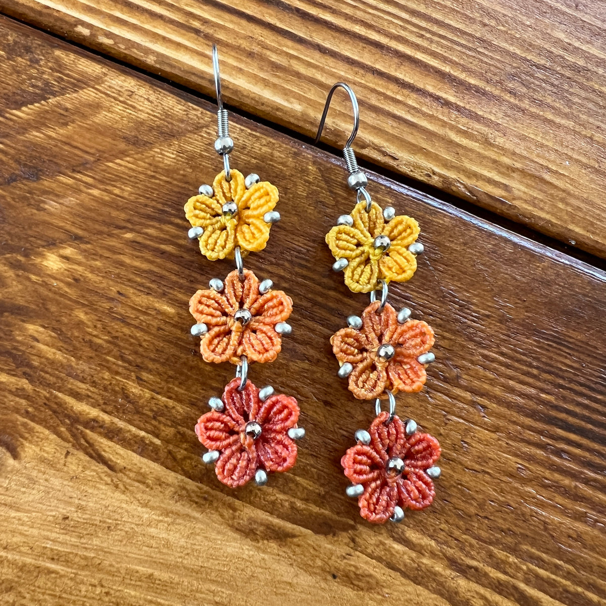 Boucles d’oreilles Blossom en micro-macramé aux couleurs de l’automne, trois fleurs jaune Soleil, orange clair Topaz et orange foncé, avec perles argentées, création artisanale Macram’Elo Créations.

