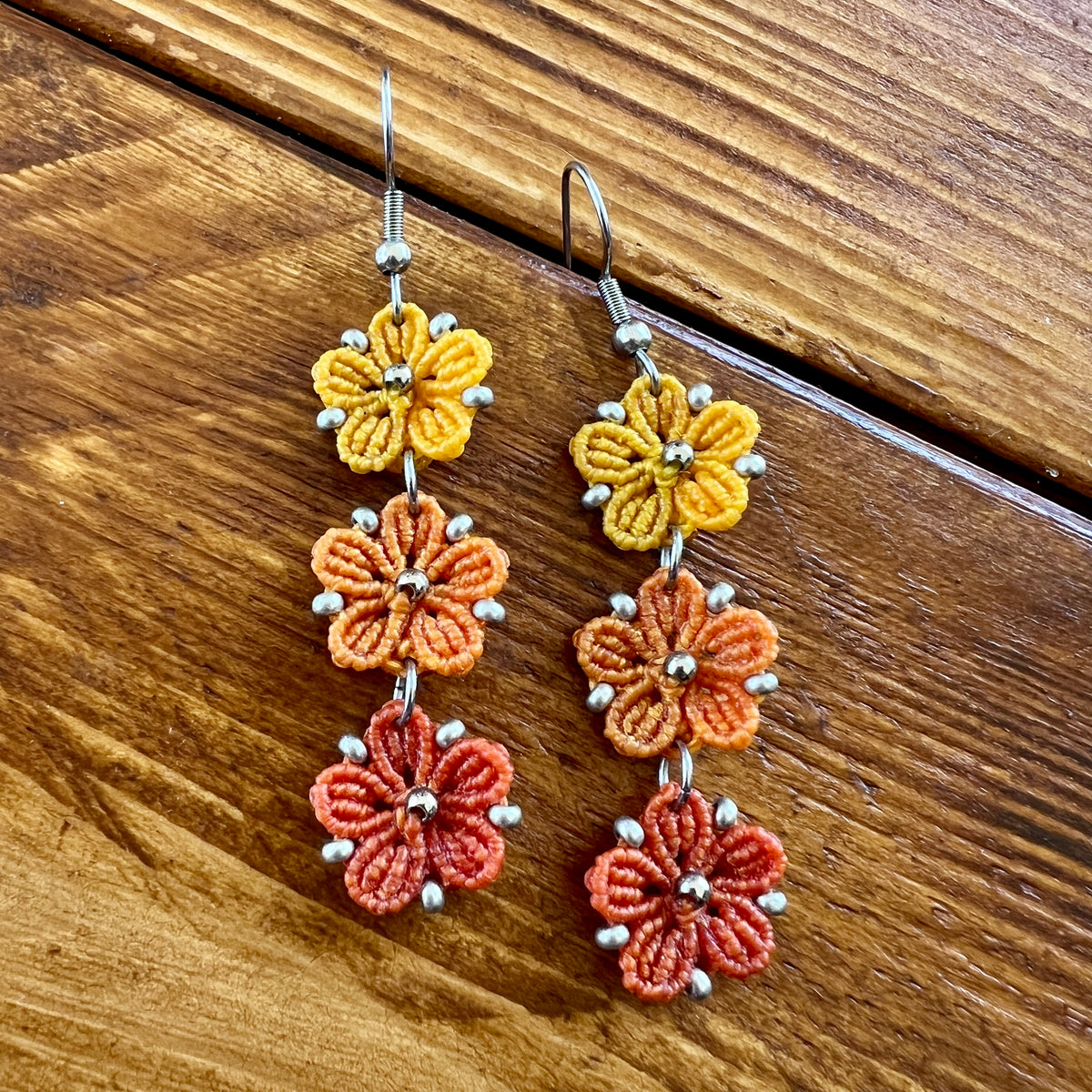 Boucles d’oreilles Blossom en micro-macramé aux couleurs de l’automne, trois fleurs jaune Soleil, orange clair Topaz et orange foncé, avec perles argentées, création artisanale Macram’Elo Créations.

