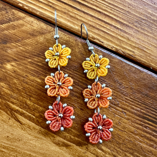 Boucles d’oreilles Blossom en micro-macramé aux couleurs de l’automne, trois fleurs jaune Soleil, orange clair Topaz et orange foncé, avec perles argentées, création artisanale Macram’Elo Créations.

