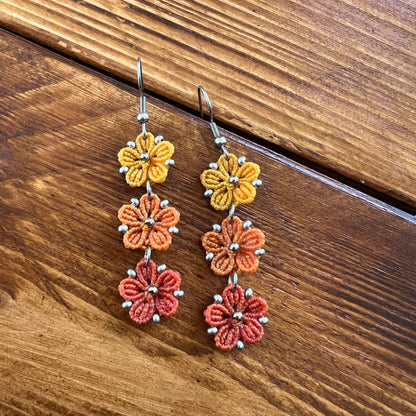 Boucles d’oreilles Blossom en micro-macramé aux couleurs de l’automne, trois fleurs jaune Soleil, orange clair Topaz et orange foncé, avec perles argentées, création artisanale Macram’Elo Créations.

