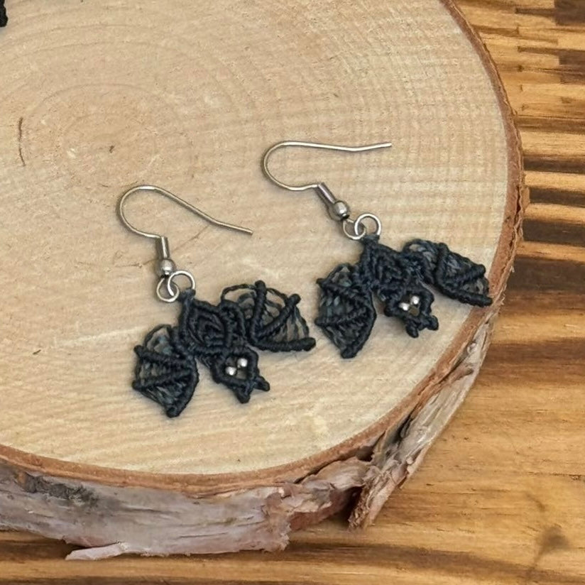 Une paire de boucles d'oreilles tissé en micro-macramé représentant des chauves-souris en coloris orage, c'est un bleu-gris foncé
