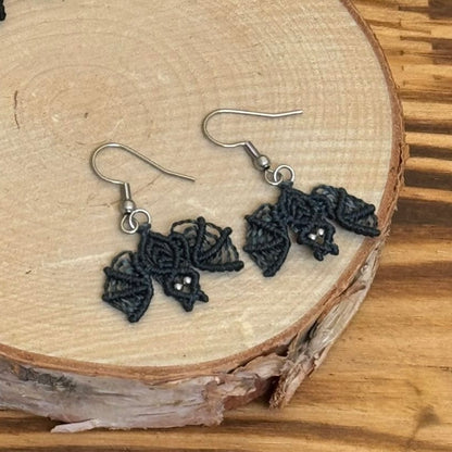 Une paire de boucles d'oreilles tissé en micro-macramé représentant des chauves-souris en coloris orage, c'est un bleu-gris foncé