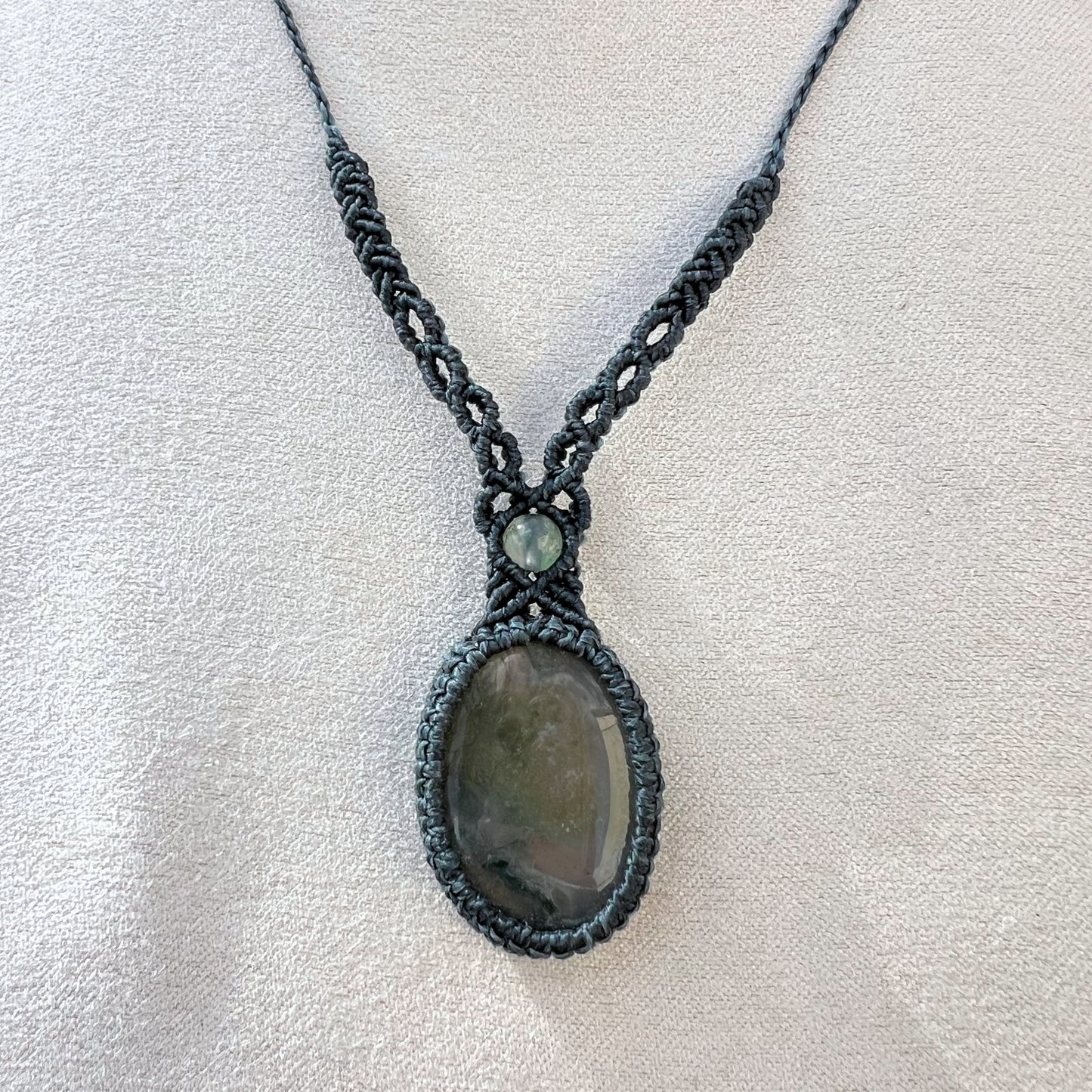 Un collier tissé en micro-macramé gris foncé avec un cabochon oval et une perle une pierre naturelle d'Agate mousse