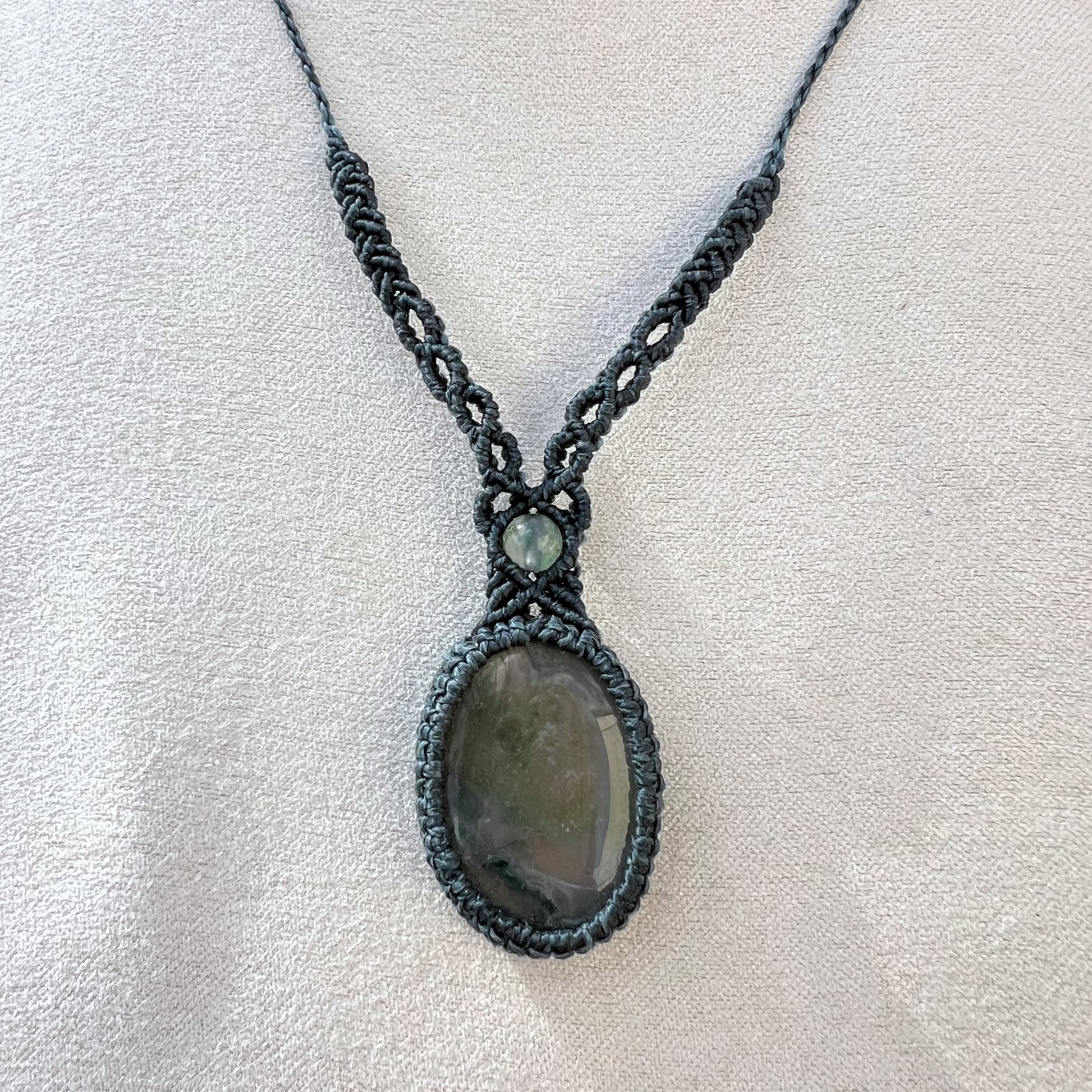 Un collier tissé en micro-macramé gris foncé avec un cabochon oval et une perle une pierre naturelle d'Agate mousse